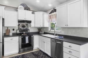 Kitchen featuring appliances with stainless steel finishes, a sink, under cabinet range hood, dark countertops, and white cabinets