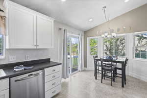 Kitchen featuring stainless steel dishwasher, vaulted ceiling, dark countertops, a chandelier, and white cabinets