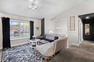 Carpeted living room featuring lofted ceiling, baseboards, ceiling fan, and a chandelier
