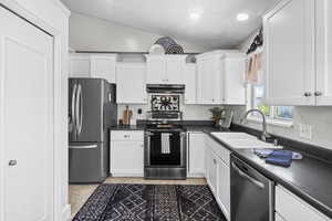 Kitchen with stainless steel appliances, under cabinet range hood, lofted ceiling, a sink, and white cabinetry