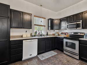 Kitchen with appliances with stainless steel finishes, a sink, pendant lighting, and light countertops