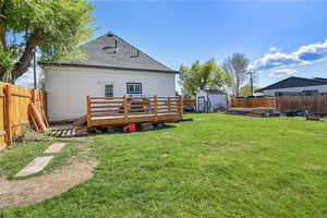 Back of house with a deck, a shed, an outbuilding, and roof with shingles