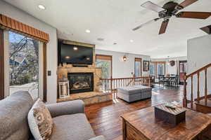 Living room with hardwood / wood-style floors, ceiling fan, a stone fireplace, a textured ceiling, and recessed lighting
