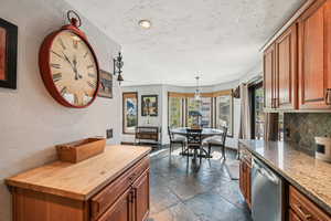 Kitchen with wooden counters, stone tile flooring, stainless steel dishwasher, tasteful backsplash, and brown cabinets