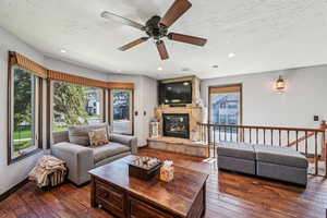 Living area featuring a textured ceiling, a stone fireplace, a ceiling fan, dark wood-style flooring, and recessed lighting