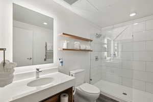 Full bathroom with toilet, a tile shower, vanity, a towel warming rack, and recessed lighting