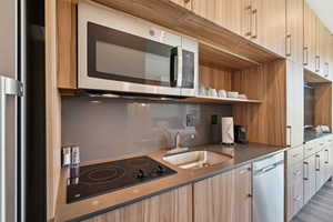 Kitchen with appliances with stainless steel finishes, modern cabinets, a sink, and light brown cabinetry