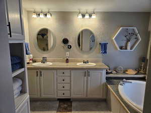 Bathroom with double vanity, a bath, and a textured wall