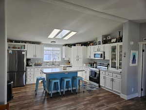 Kitchen with stainless steel appliances, a breakfast bar, white cabinetry, a skylight, and lofted ceiling