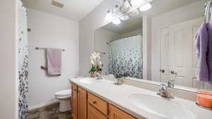Bathroom with toilet, double vanity, grab bars and stone finish floors