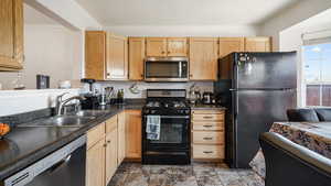 Kitchen featuring black appliances, dark countertops, a sink, light brown cabinetry, and light stone finish floors