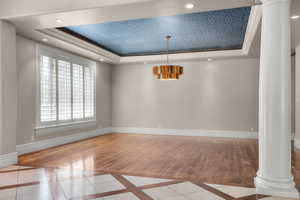 Dining area with decorative columns, a raised ceiling, inlaid floor details, baseboards, and ornamental molding