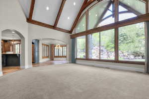 Living room featuring a chandelier, high vaulted ceiling, ornate columns, light colored carpet, and baseboards