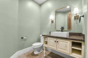 Bathroom featuring toilet, baseboards, vanity, and stone finish flooring