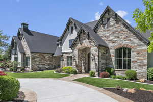 View of front facade featuring stone siding, a front lawn, a chimney, stucco siding, and a shingled roof