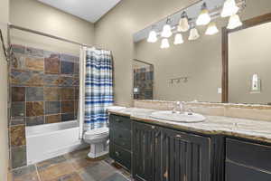 Full bathroom with vanity, toilet, shower / bath combo, and stone finish flooring