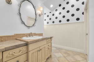 Bathroom with wallpapered walls, vanity, wainscoting, and baseboards