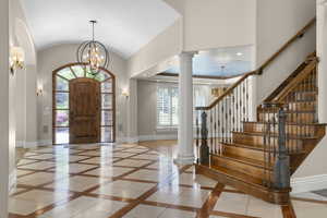 Foyer entrance featuring inlaid floor details, baseboards, ornate columns, a chandelier, and lofted ceiling