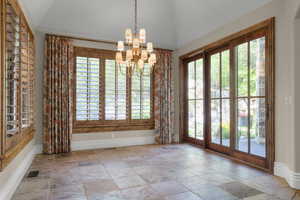 Dining area with healthy amount of natural light, a chandelier, stone tile flooring, and lofted ceiling