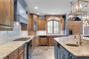 Kitchen with custom exhaust hood, stainless steel gas cooktop, a chandelier, a sink, and oven