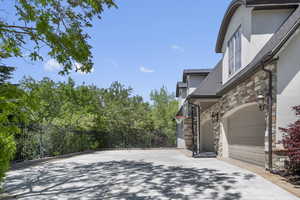 View of side of home with stone siding, stucco siding, fence, and garage