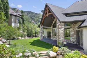 Back of property featuring roof with shingles, stone siding, a mountain view, lawn, and a patio area