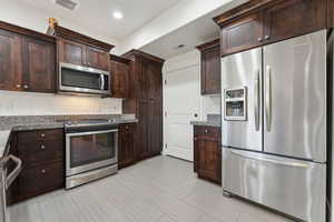 Kitchen featuring appliances with stainless steel finishes, tasteful backsplash, dark brown cabinets, dark stone countertops, and recessed lighting