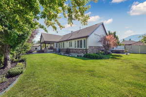 Rear view of house with a hot tub, stone siding, a patio, roof with shingles, and an outdoor living space