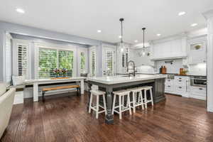 Kitchen with glass insert cabinets, tasteful backsplash, an island with sink, a kitchen bar, and dark wood-type flooring