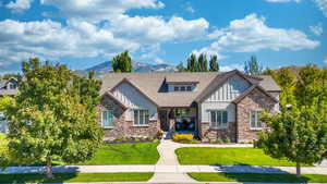 View of front facade featuring board and batten siding, stone siding, a mountain view, and a front lawn