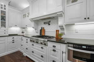 Kitchen with stainless steel appliances, white cabinets, tasteful backsplash, dark wood-style flooring, and glass insert cabinets