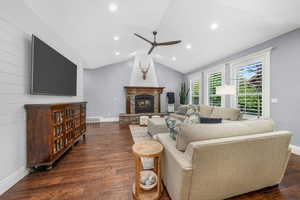 Living room with ceiling fan, a glass covered fireplace, dark wood-type flooring, recessed lighting, and lofted ceiling