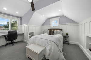 Bedroom with a decorative wall, carpet, vaulted ceiling, wainscoting, and ceiling fan