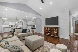 Living room featuring vaulted ceiling, dark wood finished floors, wood walls, recessed lighting, and a ceiling fan
