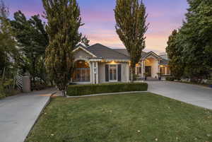 View of front facade with concrete driveway, a tiled roof, a lawn, and stucco siding