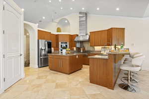 Kitchen featuring stainless steel appliances, wall chimney exhaust hood, a sink, brown cabinets, and high vaulted ceiling