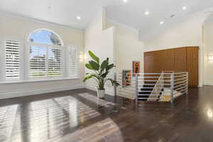Interior space featuring arched walkways, hardwood / wood-style floors, high vaulted ceiling, baseboards, and ornamental molding