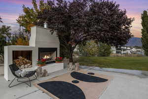 Patio terrace at dusk with a lit fireplace and a lawn