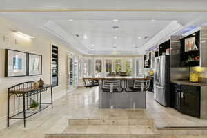 Kitchen featuring stainless steel fridge with ice dispenser, a tray ceiling, a kitchen bar, baseboards, and a kitchen island