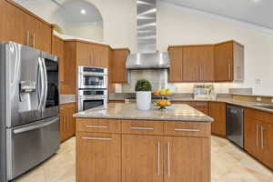 Kitchen with stainless steel appliances, wall chimney exhaust hood, a center island, light stone countertops, and ornamental molding