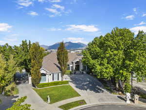 View of property hidden behind natural elements with concrete driveway, a mountain view, a tiled roof, a front yard, and a gate