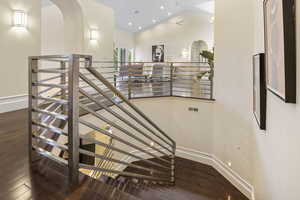 Staircase featuring arched walkways, wood-type flooring, baseboards, and lofted ceiling