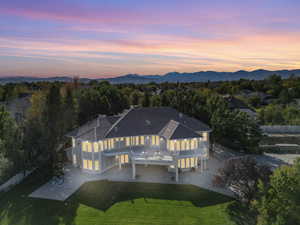 Back of house at dusk featuring a balcony, a patio, a mountain view, a tile roof, and stucco siding