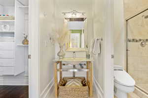 Full bath with a shower stall, toilet, and wood finished floors