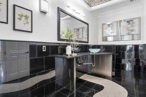 Bathroom with tile walls, granite tiled floors, wainscoting, crown molding, and vanity