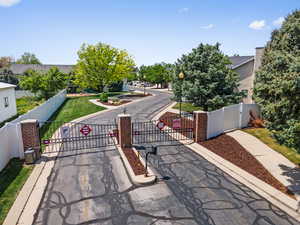 View of asphalt street featuring street lights, a gate, traffic signs, curbs, and a gated entry