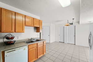Kitchen featuring white appliances, a sink, a textured ceiling, light tile patterned floors, and baseboards