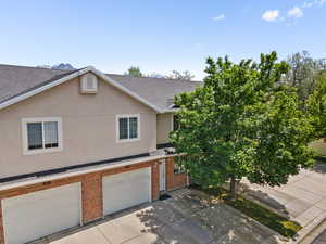View of property with brick siding, a shingled roof, stucco siding, concrete driveway, and an attached garage