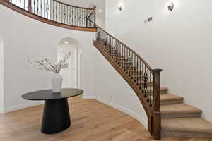 Stairway featuring wood finished floors, baseboards, arched walkways, and a towering ceiling