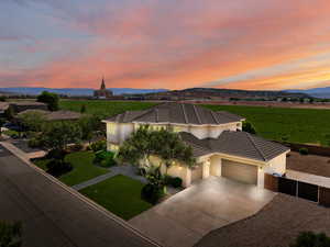 View of front facade featuring a garage, driveway, stucco siding, a tiled roof, and a rural view